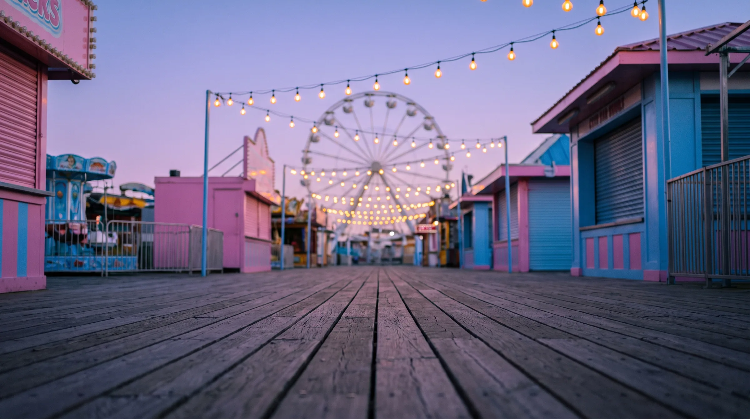 An empty boardwalk at dusk, ferris wheel lit at the end of it