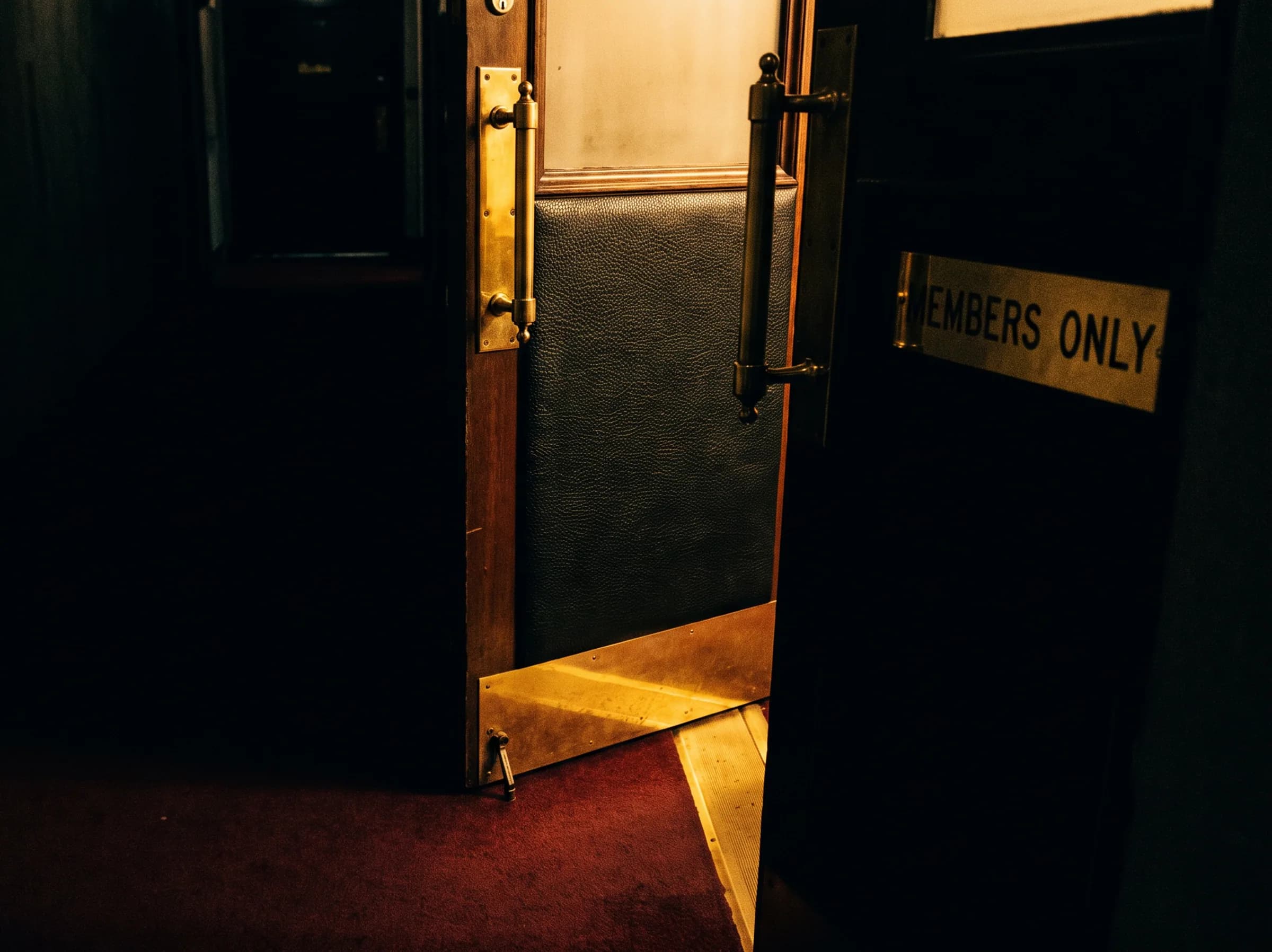 A members-only door standing ajar at the end of a dark corridor