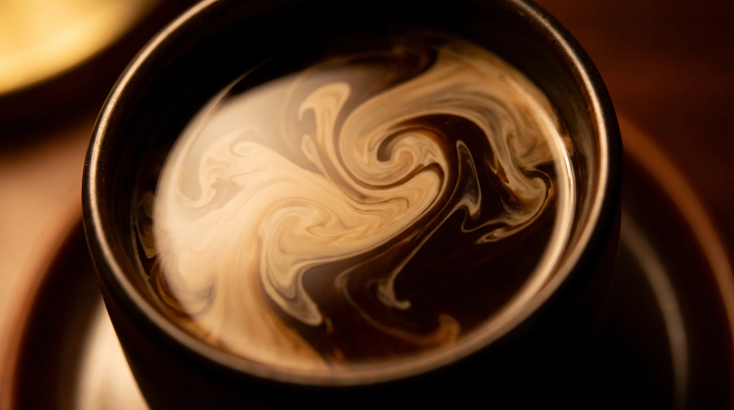Cream folding through dark coffee, seen from above