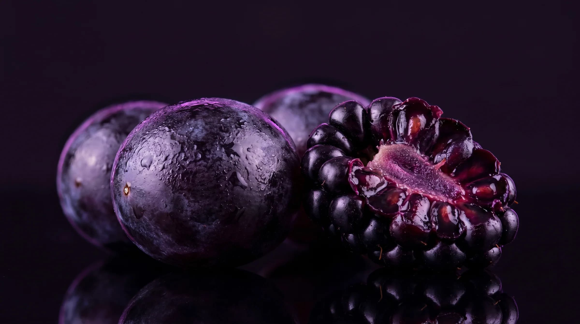 Dark grapes and a split blackberry on black, lit purple